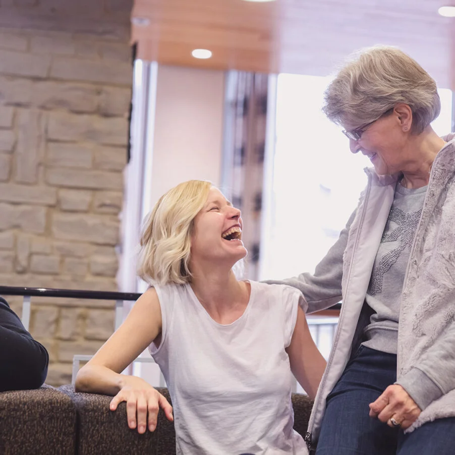 Kaksi nuorempaa ja yksi vanhempi nainen nauraa sohvalla.
