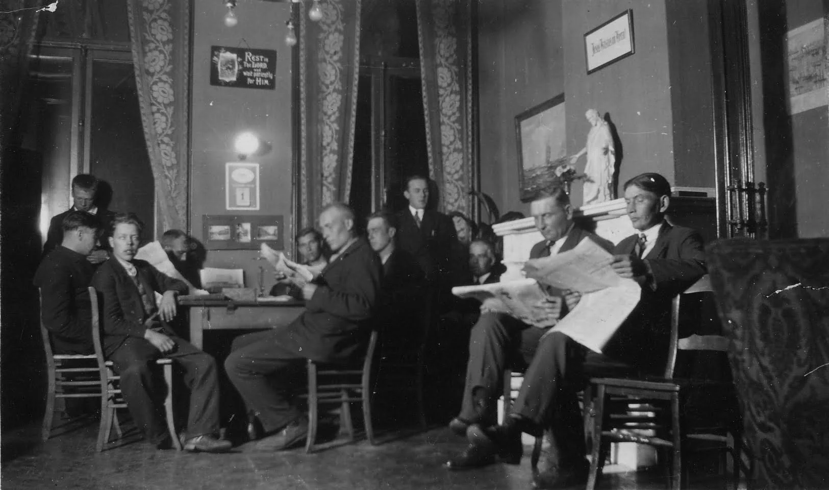 "Siististi pukeutuneita miehiä istuu ja lukee sanomalehtiä. Mustavalkokuva."