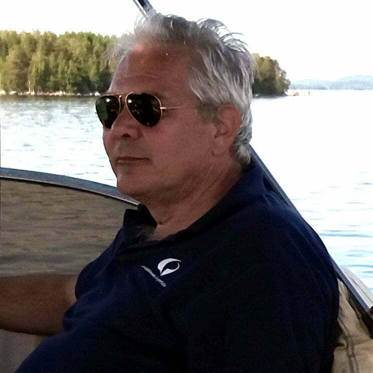 "Silmälasipäinen siniseen paitaan pukeutunut mies istuu veneessä."