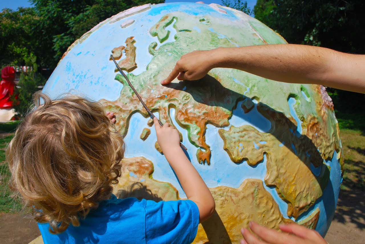 Iso karttapallo, jonka äärellä aikuisen sormi osoittaa Eurooppaa ja lapsi katsoo vieressä.
