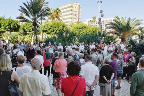 Suuri joukko ihmisiä kokoontueena aukiolle, jota ympäröivät vihreät palmut.