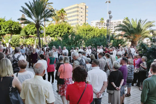 Suuri joukko ihmisiä kokoontueena aukiolle, jota ympäröivät vihreät palmut.