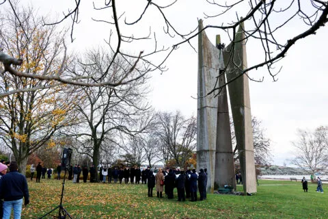 Ihmisiä kokoontunut korkean betonisen muistomerkin äärelle syksyisellä ilmalla.