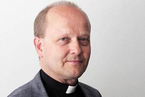 Papinpaitaan pukeutunut hymyilevä mies.