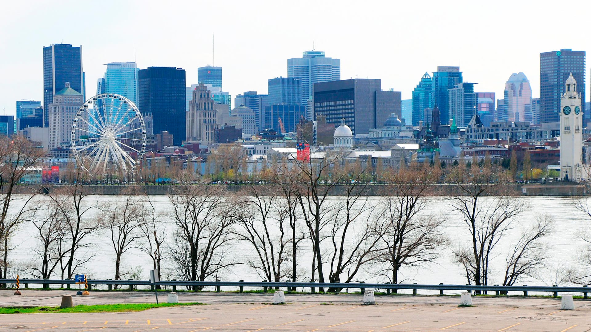 Joki, jonka vastarannalla kaupungin silhuetti päivällä, vasemmalla maailmanpyörä.