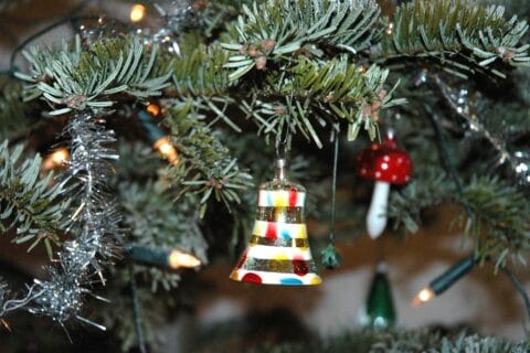 Kuusen oksia, joissa roikkuu kellomainen joulukoriste ja kynttilöitä.