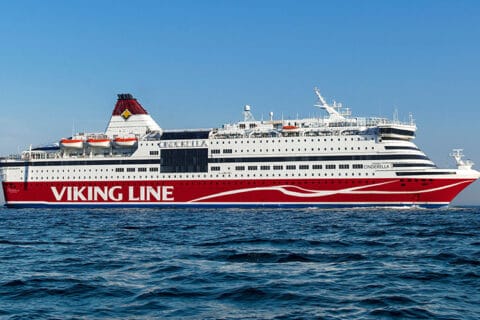 Punavalkoinen iso laiva horisontissa, alla sininen meri ja yläpuolella sininen taivas.