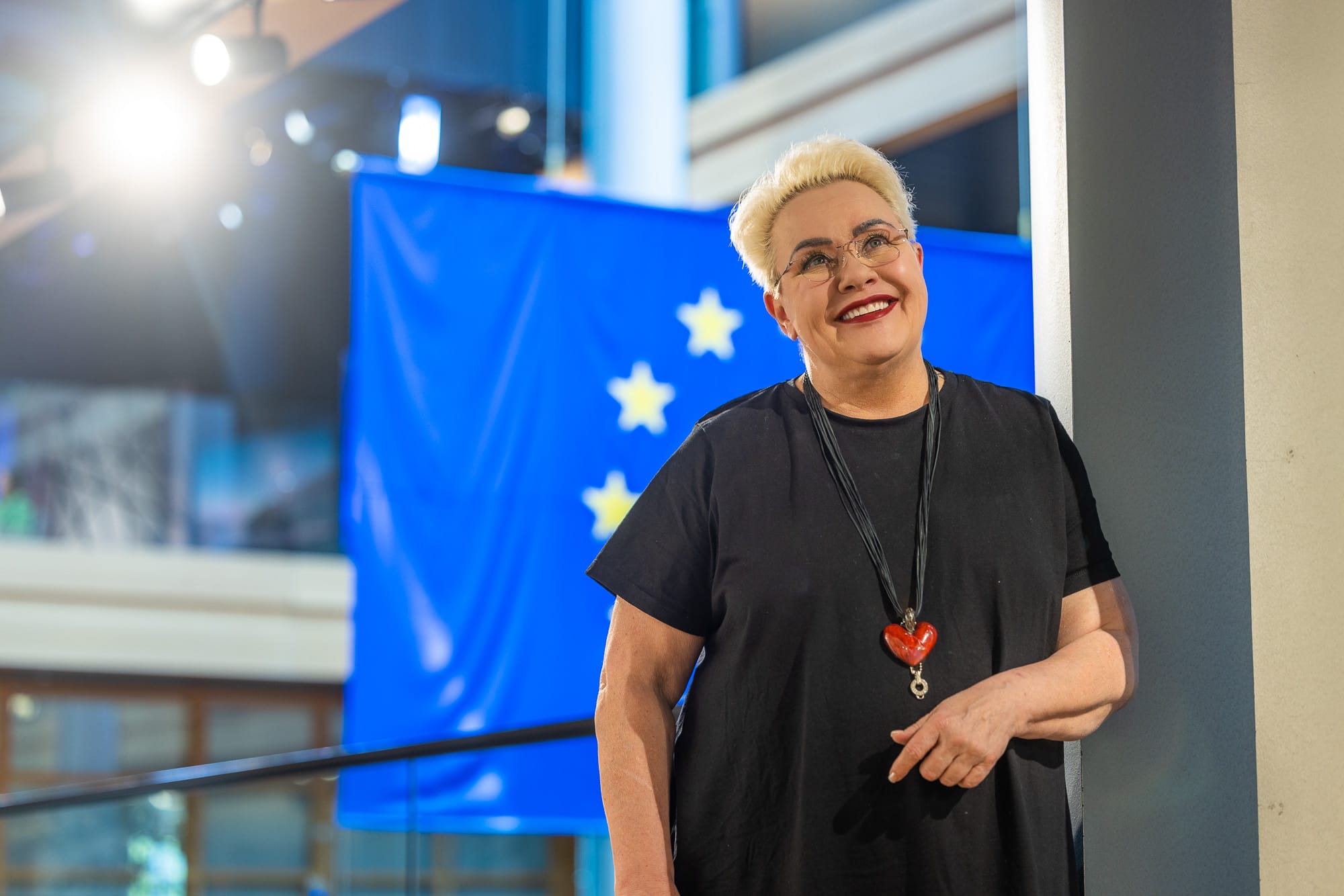 Hymyilevä vaaleatukkainen nainen seisoo Euroopan unionin lipun edessä.